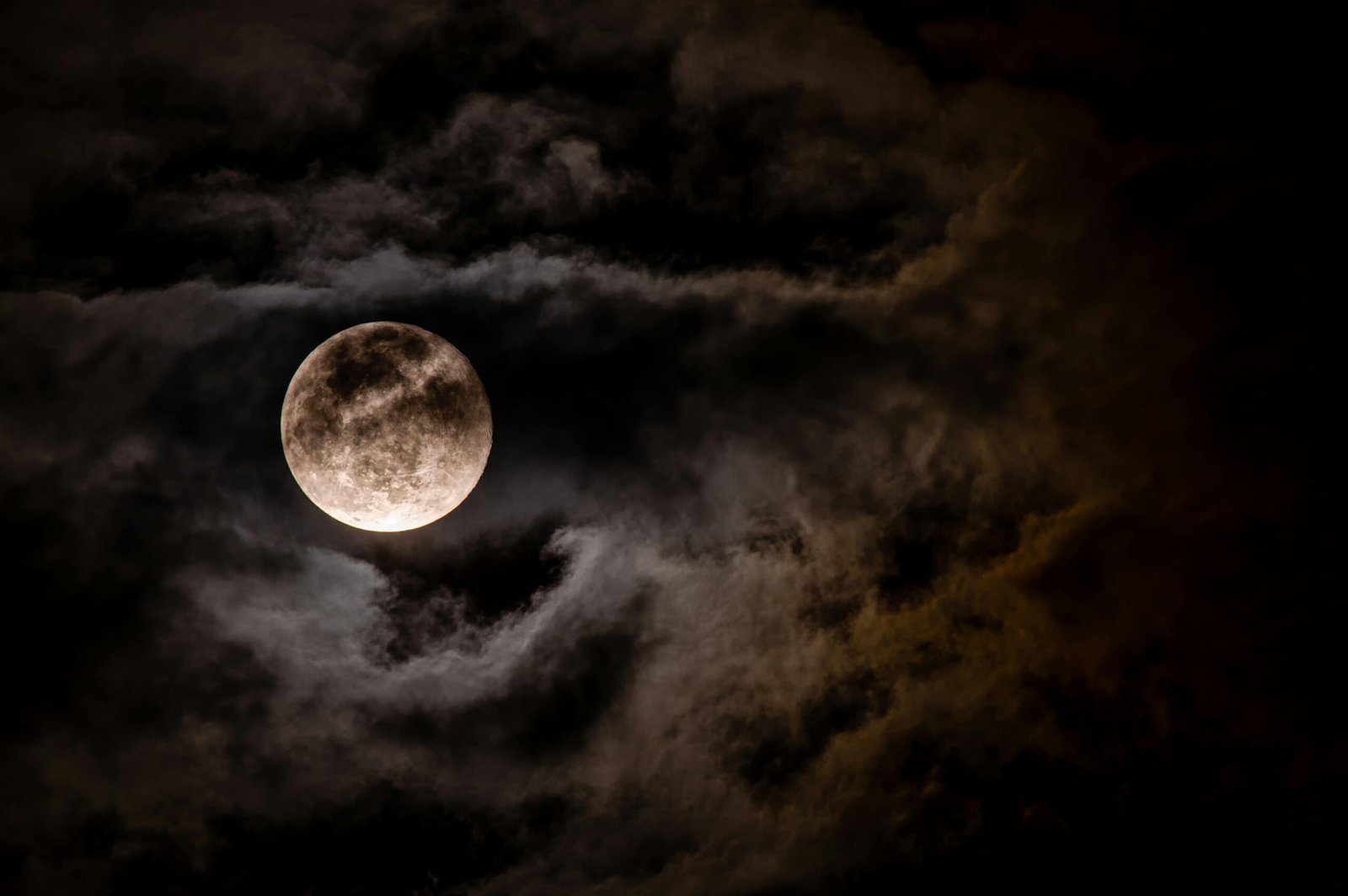 Captivating full moon obscured by dark clouds in a night sky, creating a mysterious ambiance.